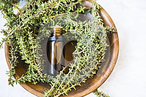 Thyme essential oil bottle with thyme herb twigs in wooden plate top view