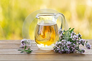 Thyme essential oil in a glass jug and branches of a fresh thyme plant with flowers on a wooden background. Copy space