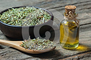 Thyme essential oil and Heap of dry thyme in wooden spoon and in bowl on wooden background