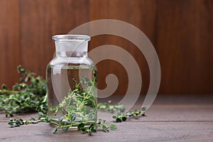 Thyme essential oil on wooden table, space for text