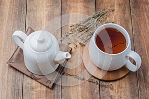 Thyme herbal tea. White cup on a bamboo support and a teapot on a napkin on a wooden table. Top view