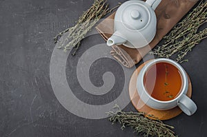 Thyme herbal tea in a white cup and kettle on a black stone table. Copyspace and top view