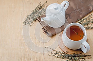 Thyme herbal tea in a white cup and teapot on a wooden table. Copyspace and top view