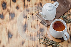 Thyme herbal tea in a white cup and teapot on a wooden table. Copyspace and top view