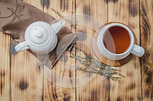 Thyme herbal tea in a white cup and teapot on a wooden table, top view