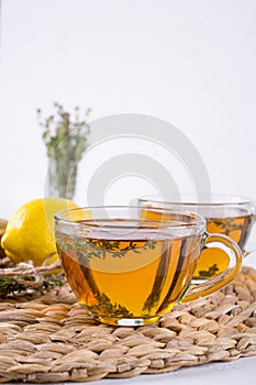 Thyme tea in glass cup, sprig of fresh thyme, lemon and ginger on white table