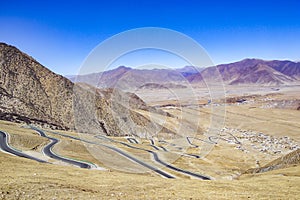Tibet landscape showing a road through the mountains on a blue sky day, near the city of Lhasa.