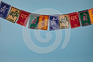 Tibetan Buddhist flags against blue background. Text on flags Om mani padme hum meaning The jewel is in the lotus.