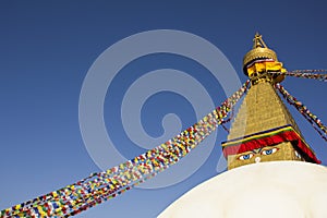 A Tibetan Buddhist Stupa Boudhanath with eyes and multicolored prayer flags against a clean blue sky