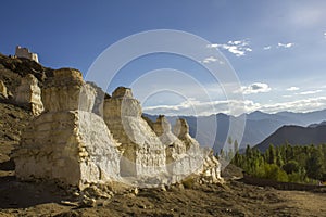 A Tibetan Buddhist white temples of stupa on a stony hillside against the backdrop of a mountain valley under a blue sky and white