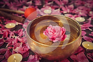 Tibetan singing bowl with floating inside in water pink peony flower. Burning candles, special sticks and petals on the black ston