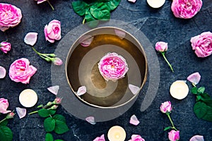 Tibetan singing bowl with floating rose inside. Burning candles, tea rose flowers and petals on the black stone background. Medita