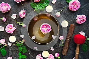 Tibetan singing bowl with floating rose inside. Burning candles, tea rose flowers and petals on the black stone background. Medita