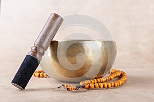 Tibetan singing bowl with stick, mala beads strands used during mantra meditations on beige stone background