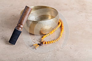 Tibetan singing bowl with stick, mala beads strands used during mantra meditations on beige stone background