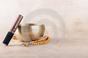 Tibetan singing bowl with stick, mala beads strands used during mantra meditations on beige stone background