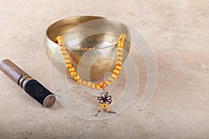 Tibetan singing bowl with stick, mala beads strands used during mantra meditations on beige stone background