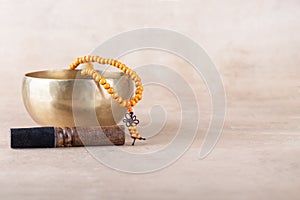 Tibetan singing bowl with stick, mala beads strands used during mantra meditations on beige stone background