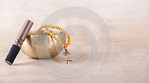 Tibetan singing bowl with stick, mala beads strands used during mantra meditations on beige stone background