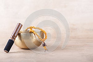 Tibetan singing bowl with stick, mala beads strands used during mantra meditations on beige stone background