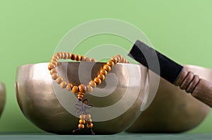 Tibetan singing bowl with stick, mala beads strands used during mantra meditations on green background