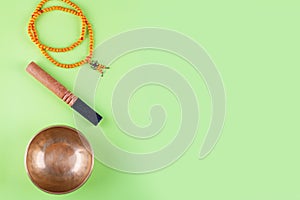 Tibetan singing bowl with stick, mala beads strands used during mantra meditations on green stone background