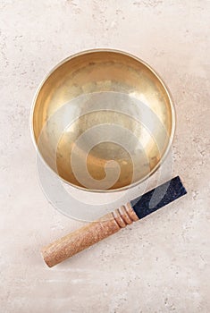 Tibetan singing bowl with sticks used during mantra meditations on beige stone background, top view, flat lay