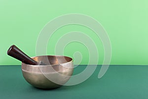 Tibetan singing bowl with sticks used during mantra meditations on green background, close up