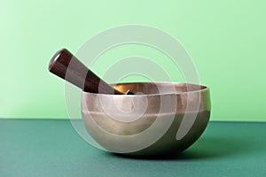 Tibetan singing bowl with sticks used during mantra meditations on green background, close up