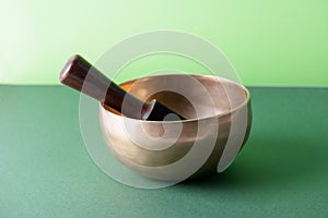 Tibetan singing bowl with sticks used during mantra meditations on green background, close up