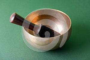 Tibetan singing bowl with sticks used during mantra meditations on green background, close up