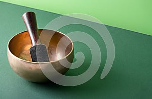 Tibetan singing bowl with sticks used during mantra meditations on green background, close up