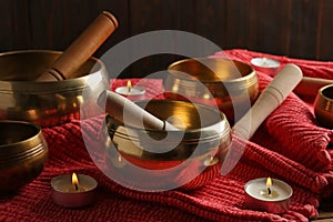 Tibetan singing bowls with mallets and burning candles on red fabric