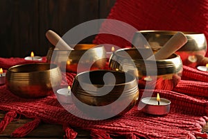 Tibetan singing bowls with mallets, burning candles and red fabric on wooden table