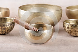 Tibetan singing bowls with sticks used during mantra meditations on beige stone background, close up