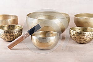 Tibetan singing bowls with sticks used during mantra meditations on beige stone background, close up