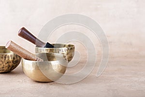 Tibetan singing bowls with sticks used during mantra meditations on beige stone background, copy space.