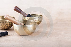 Tibetan singing bowls with sticks used during mantra meditations on beige stone background, copy space.