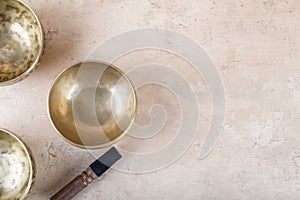 Tibetan singing bowls with sticks used during mantra meditations on beige stone background, top view, copy space