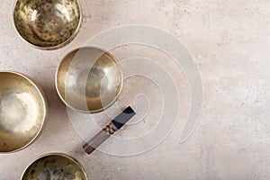 Tibetan singing bowls with sticks used during mantra meditations on beige stone background, top view, copy space