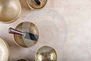 Tibetan singing bowls with sticks used during mantra meditations on beige stone background, top view, copy space