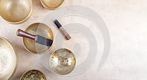 Tibetan singing bowls with sticks used during mantra meditations on beige stone background, top view, copy space