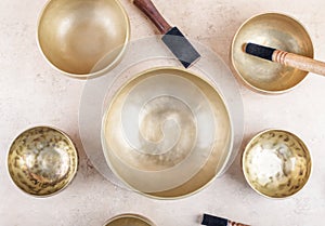 Tibetan singing bowls with sticks used during mantra meditations on beige stone background, top view, flat lay