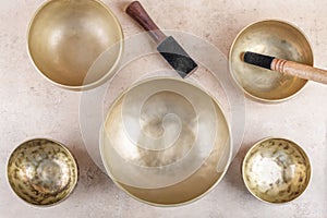 Tibetan singing bowls with sticks used during mantra meditations on beige stone background, top view, flat lay