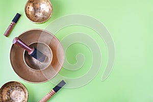 Tibetan singing bowls with sticks, used during mantra meditations on green background, flat lay, web banner