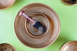 Tibetan singing bowls with sticks, used during mantra meditations on green background, flat lay, web banner