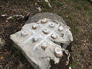 Tic-tac-toe grid and noughts and crosses marked on a rock with white paint