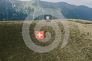 Ticino, Switzerland - August 5, 2019: Suspened cube by Jaya Schurch and siwss flag on Monte Tamaro photo