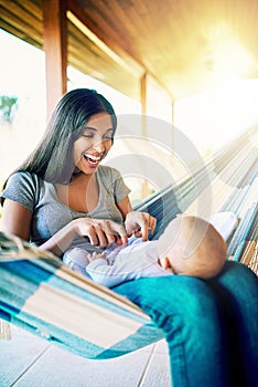 Tickle tickle. a cheerful young mother relaxing on a hammock with her infant son outside at home during the day.