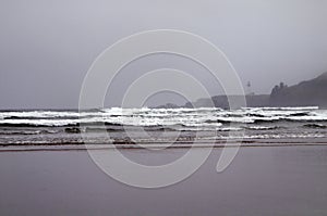 Tide of the Pacific Ocean rolling in along the sandy beach with the lighthouse visible